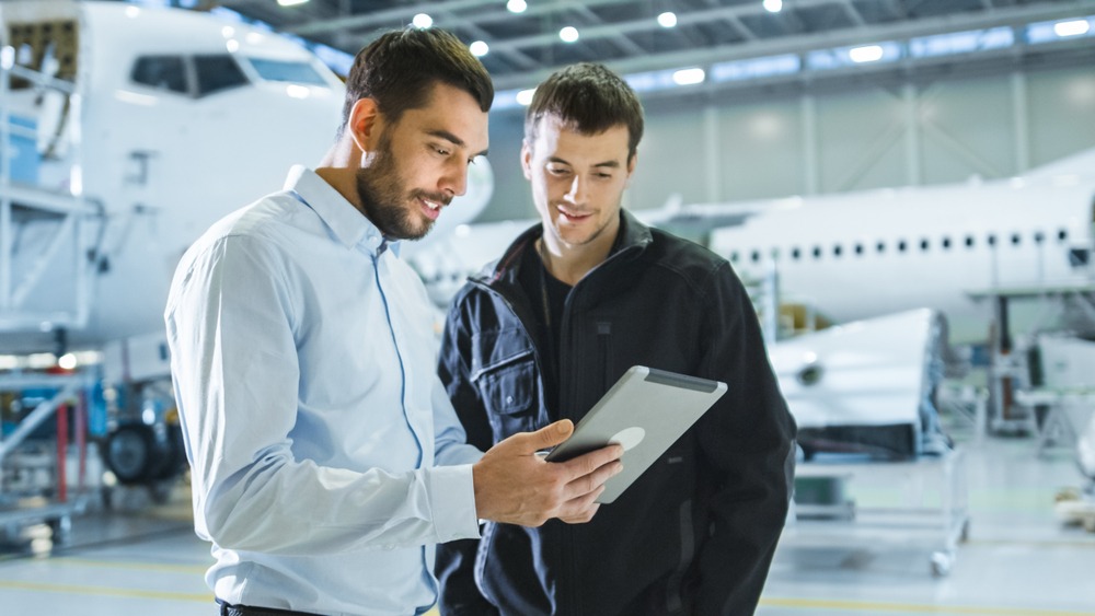 two men in aircraft hanger smiling and looking at an ipad